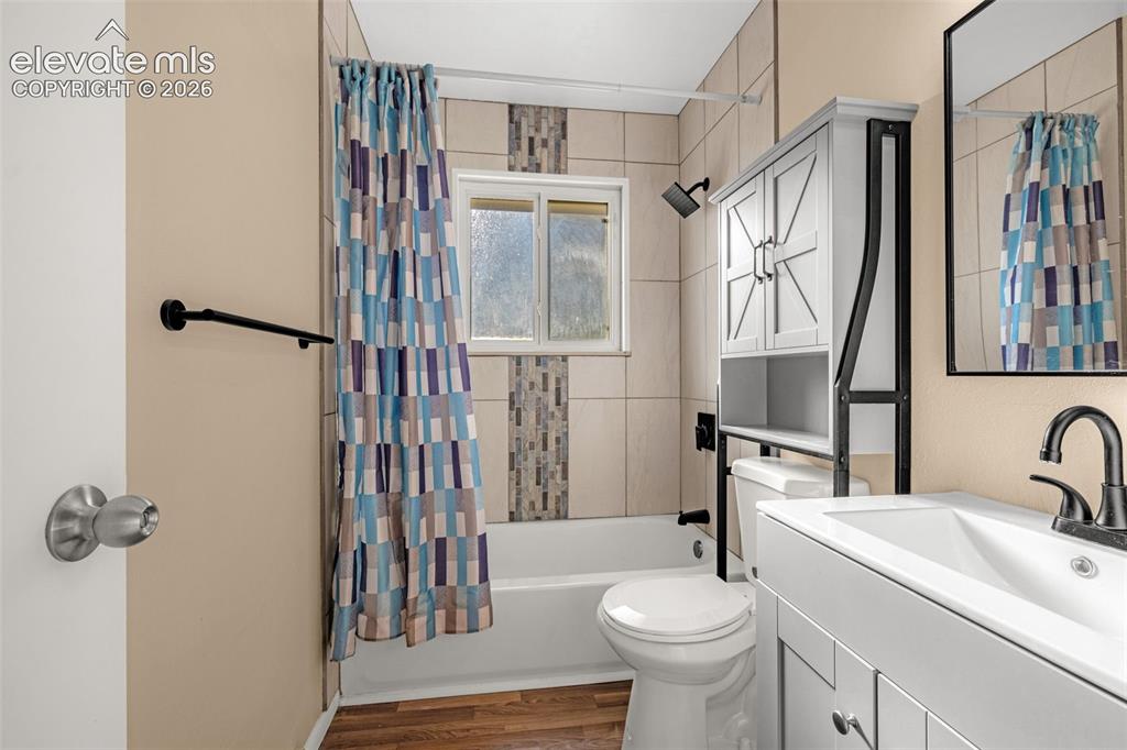 Image 8 of 27: White tub with tile surround, laminate wood-finish flooring, and a window f