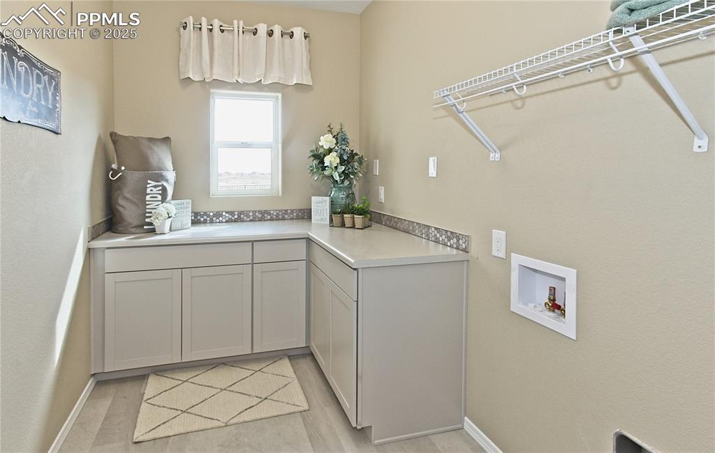 Image 5 of 25: Laundry area with washer hookup, cabinet space, and light wood finished flo