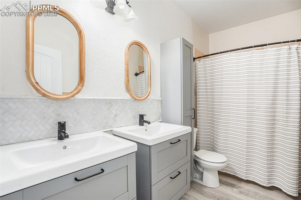 Image 20 of 24: Full bath with two vanities, light wood-style floors, tasteful backsplash, 