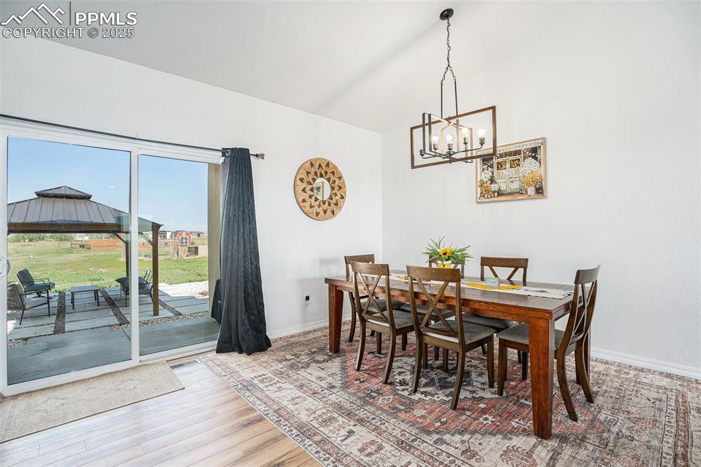 Image 7 of 24: Dining room with light wood finished floors, a chandelier, and high vaulted