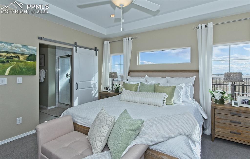 Image 16 of 30: Carpeted bedroom featuring a barn door, ensuite bath, ceiling fan, and a ra
