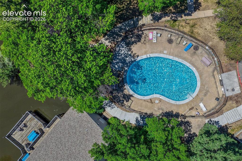 Image 25 of 35: Kidney-shaped swimming pool with a concrete deck, surrounded by mature tree