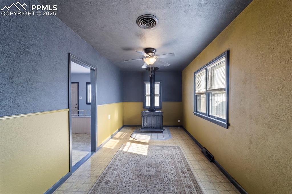 Image 10 of 41: Empty room with a textured wall, a wood stove, ceiling fan, and a textured 