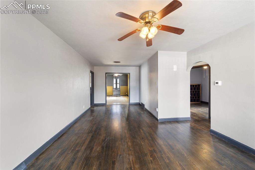 Image 5 of 41: Unfurnished room with dark wood-type flooring, ceiling fan, and arched walk