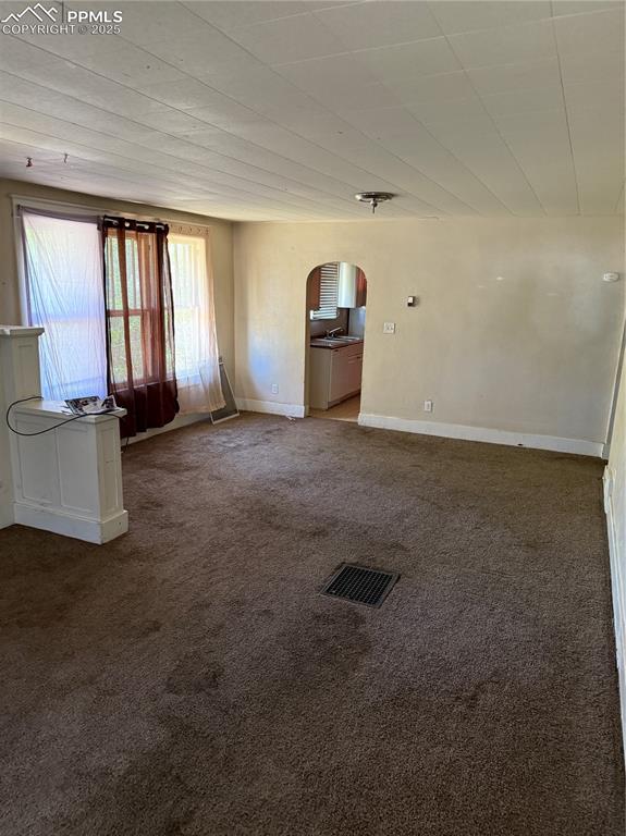 Image 3 of 11: Unfurnished living room featuring arched walkways and dark carpet