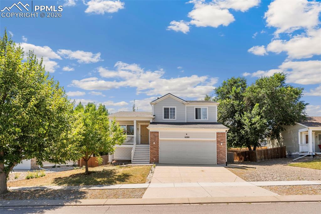 Caption: View of front of property featuring driveway, brick siding, a garage, and a porch
