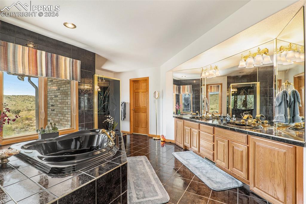 Image 28 of 50: Bathroom with a relaxing tiled bath, tile flooring, vanity with extensive c