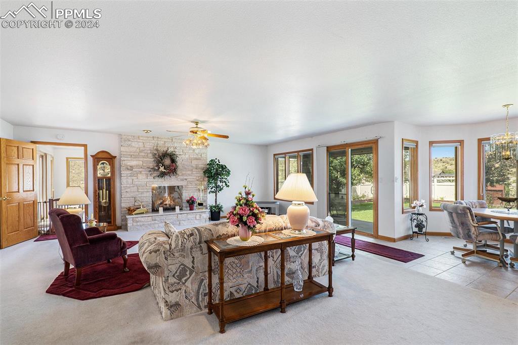 Image 8 of 50: Carpeted living room featuring a stone fireplace and ceiling fan with notab