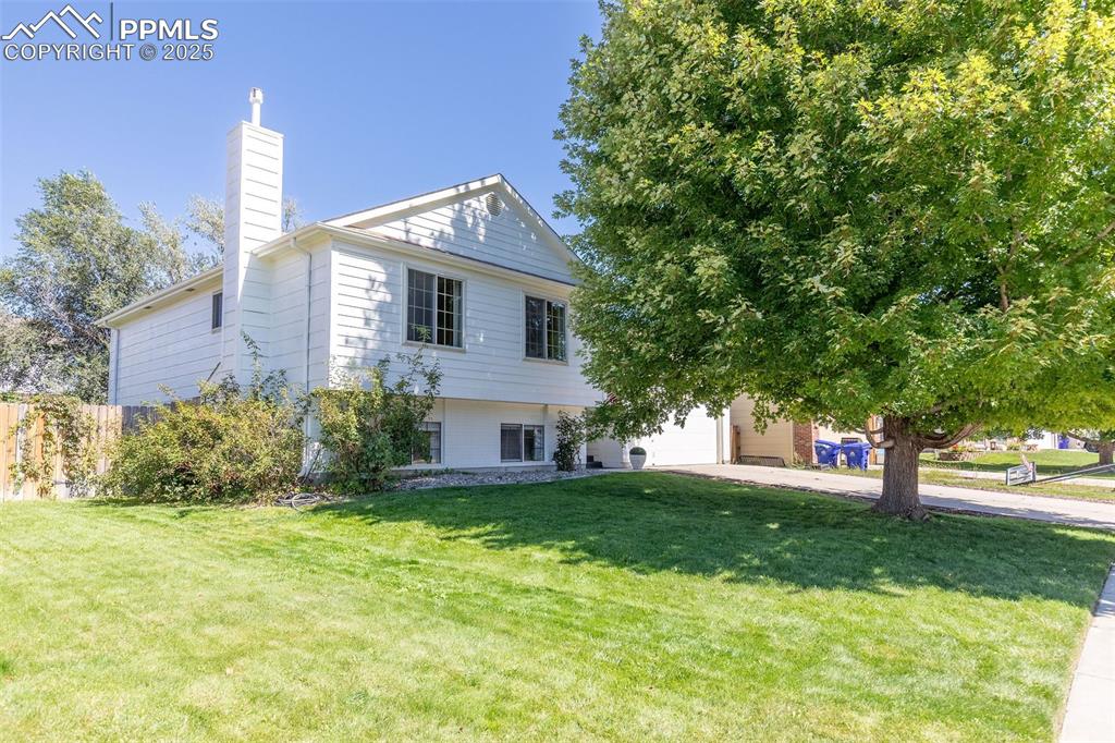 Caption: View of front facade featuring a front lawn, a chimney, and driveway