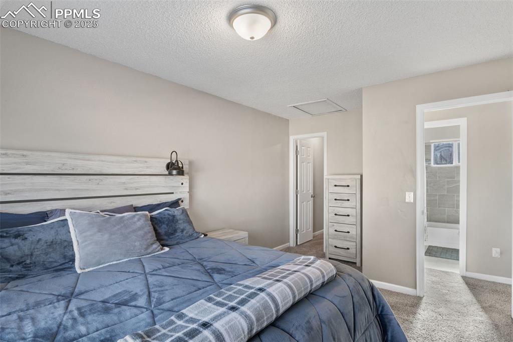 Image 16 of 38: Carpeted bedroom featuring a textured ceiling, attic access, and ensuite ba