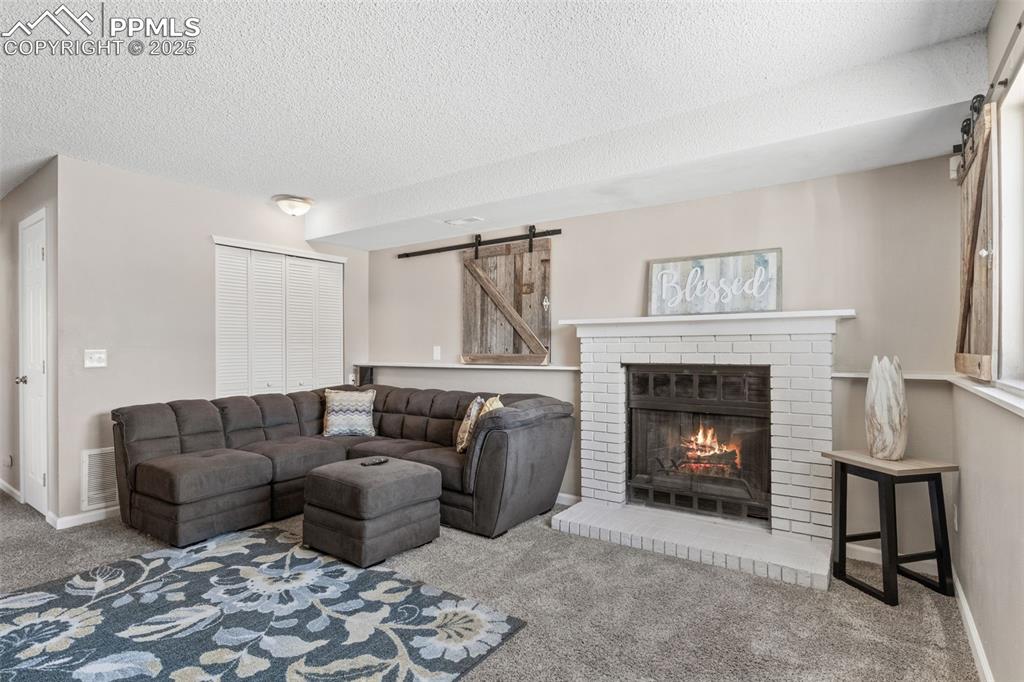 Image 20 of 38: Living room with a barn door, carpet flooring, a fireplace, and a textured