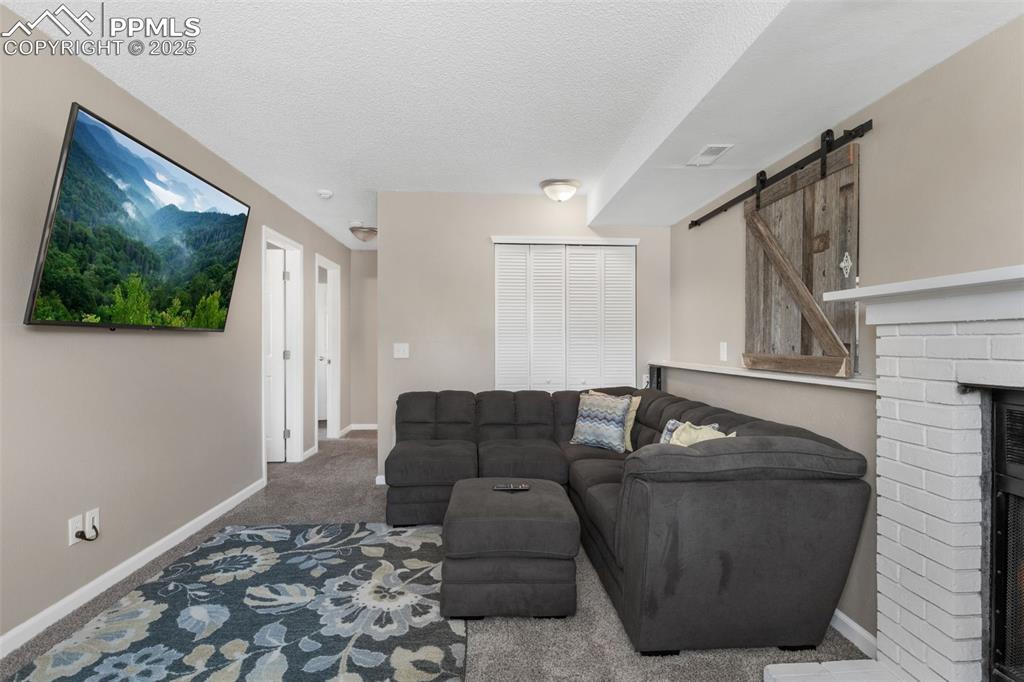 Image 22 of 38: Carpeted living area with a barn door, a textured ceiling, and a fireplace