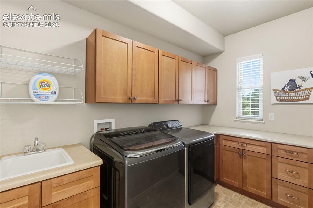 Image 19 of 47: Dedicated laundry space featuring extensive cabinetry, integrated sink, cou