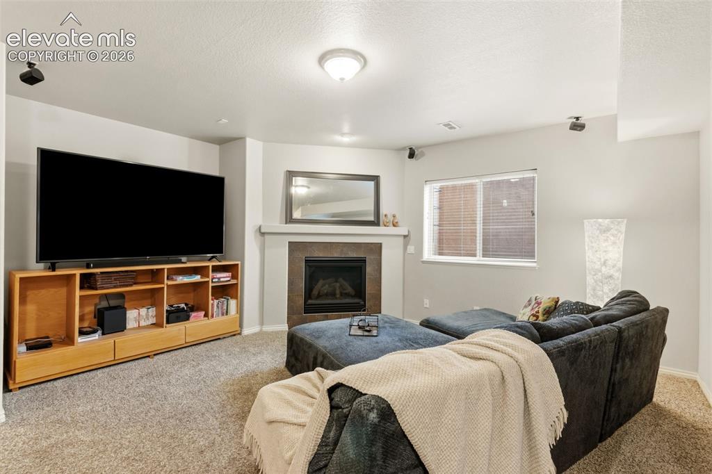 Image 32 of 47: Carpeted living space featuring a fireplace with stone surround and mantle,