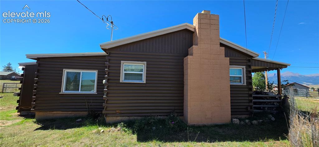 Image 27 of 35: Log-style siding exterior with a prominent block chimney and covered porch