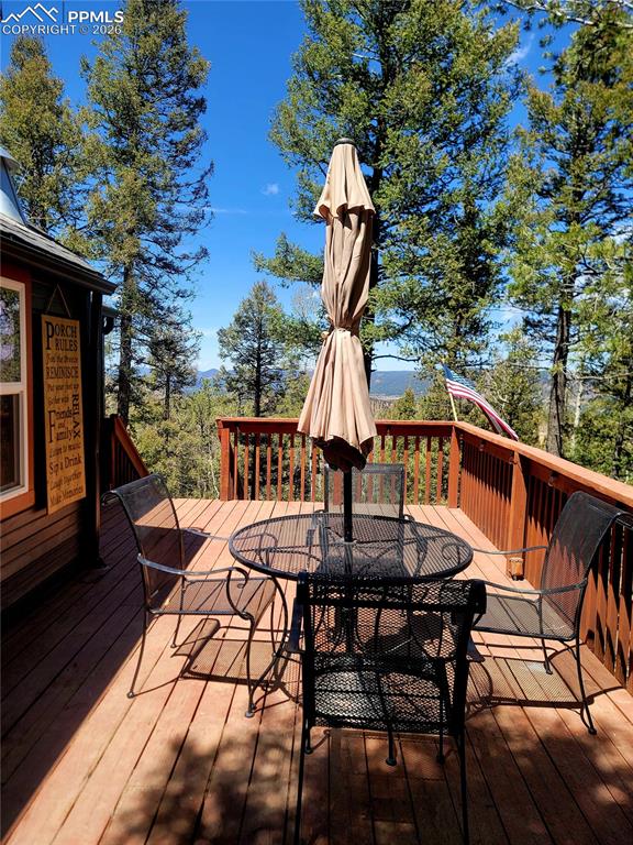 Image 8 of 21: Expansive wood-finish deck with a wood railing, surrounded by mature trees
