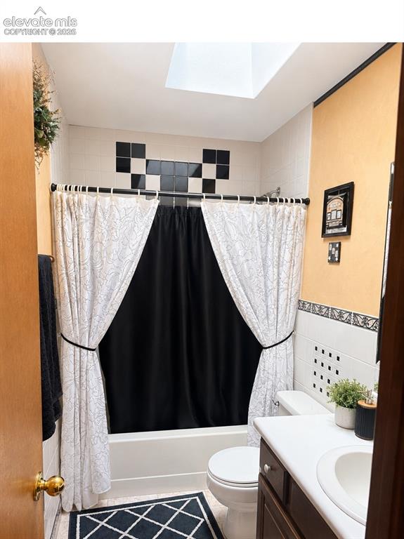 Image 14 of 20: Bathroom featuring a white bathtub, skylight, and white tile walls with bla