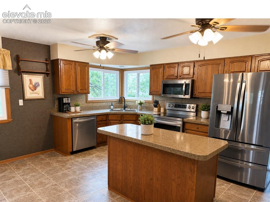 Image 6 of 20: Spacious kitchen featuring an island, wood cabinetry, stainless steel appli