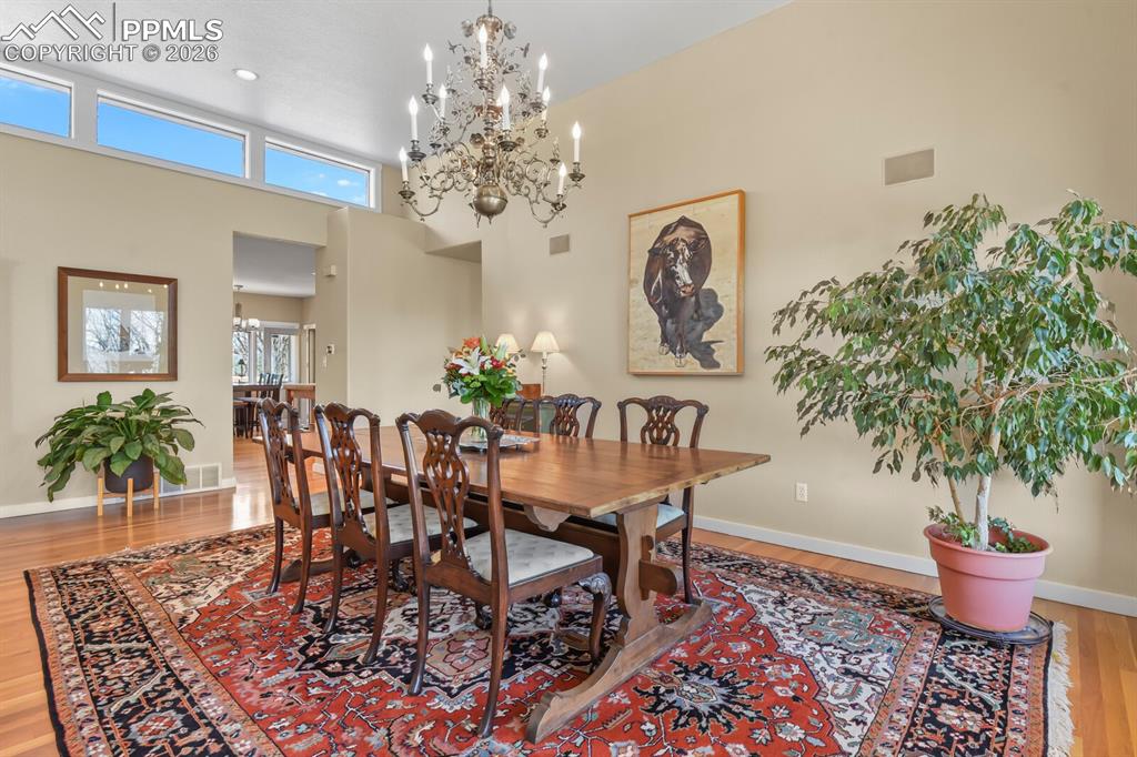 Image 14 of 50: Dining room with light wood finished floors, chandelier, and high ceilings.