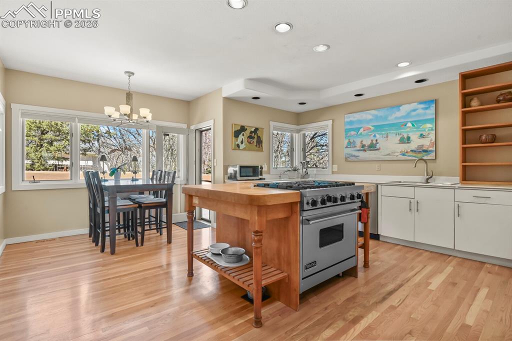 Image 15 of 50: Spacious gourmet kitchen with white cabinetry, open shelves, 6-gas burner V