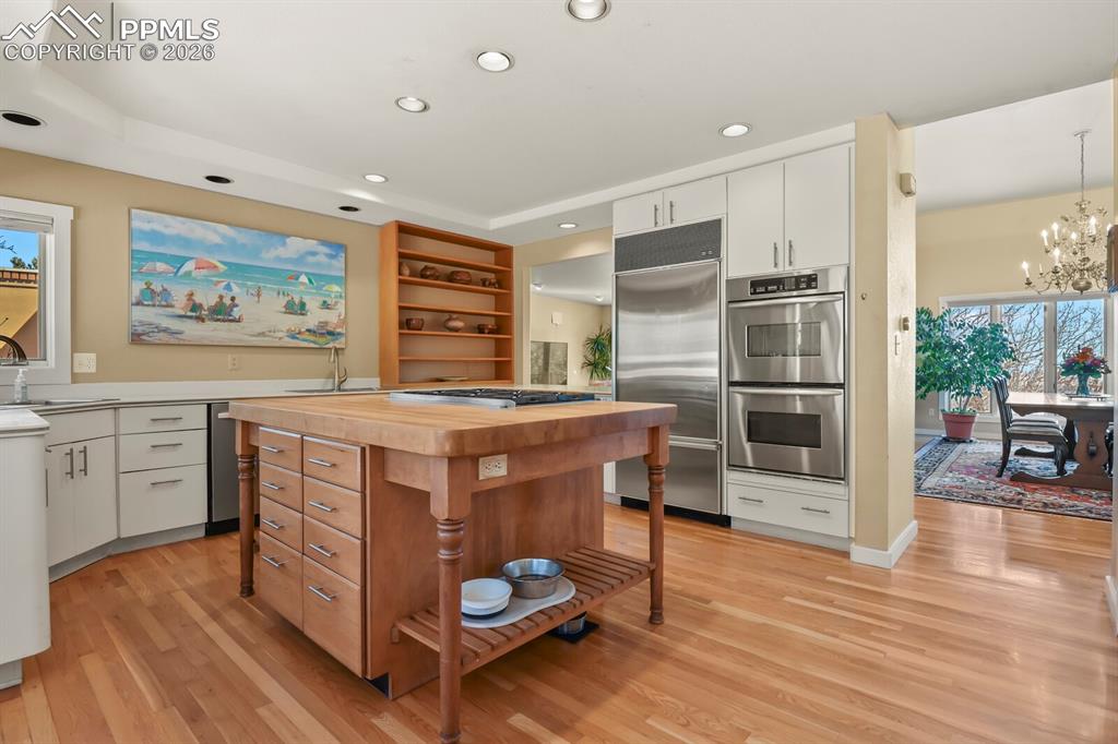 Image 16 of 50: Kitchen with white cabinetry, open shelves, stainless steel double ovens, b