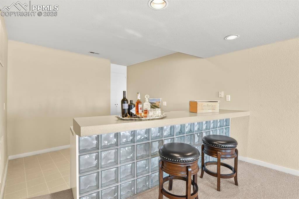 Image 35 of 50: Indoor bar with light countertops and tiled area behind the bar and some re