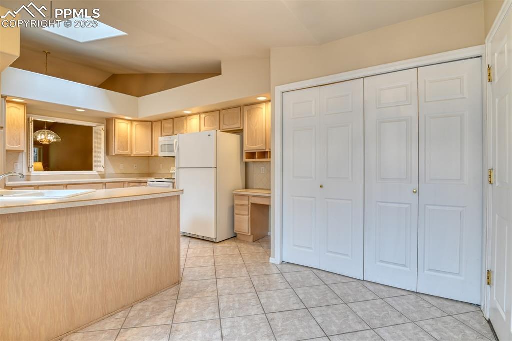 Image 10 of 37: Kitchen with a skylight, white appliances, vaulted ceiling, light counterto