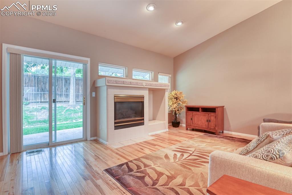 Image 19 of 37: Living area with hardwood / wood-style floors, a tiled fireplace, vaulted c