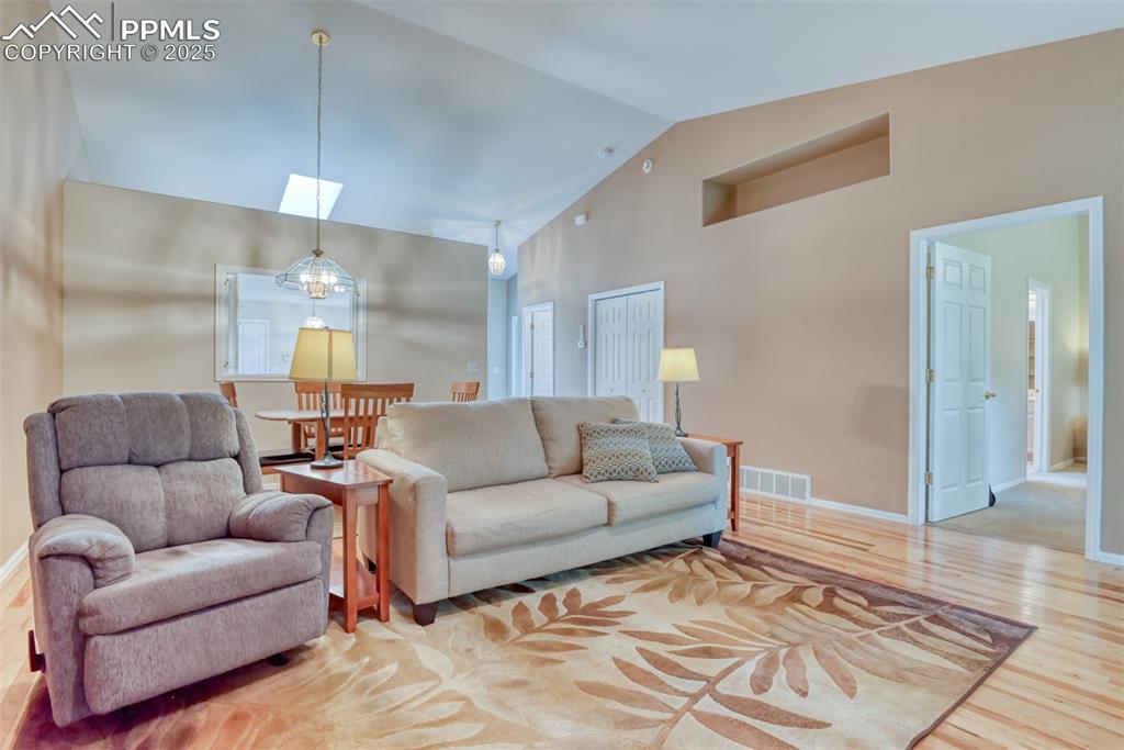 Image 21 of 37: Living room with light wood-style flooring and high vaulted ceiling