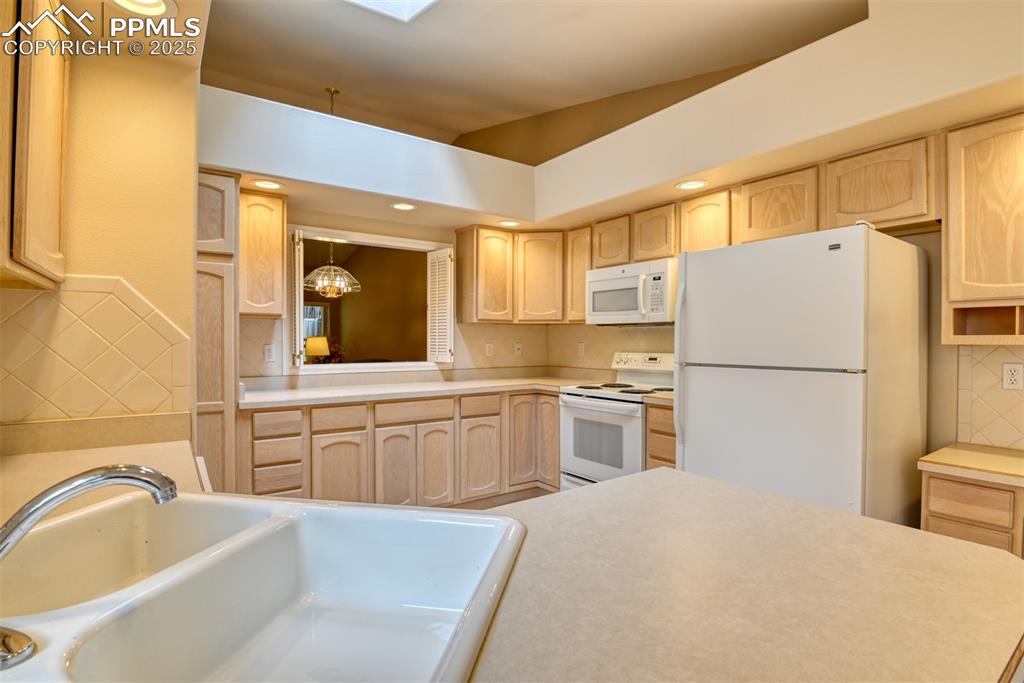 Image 7 of 37: Kitchen with decorative backsplash, light brown cabinets, white appliances,