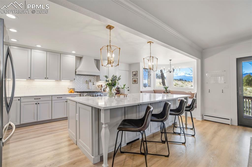 Image 12 of 49: Kitchen with light wood finished floors, a chandelier, a breakfast bar, a l