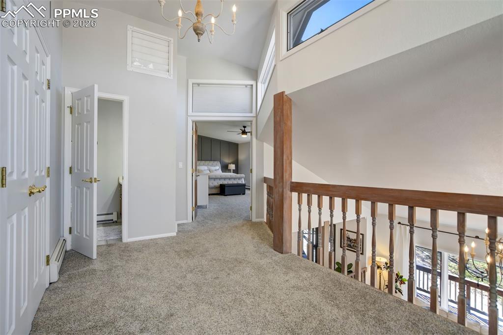 Image 25 of 49: Hall with light carpet, hanging lights, a baseboard radiator, and vaulted c