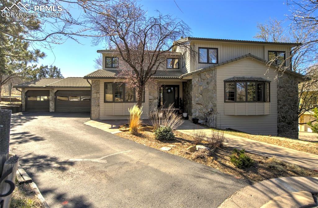 Image 3 of 49: View of front of property with stone siding, asphalt driveway, an attached 