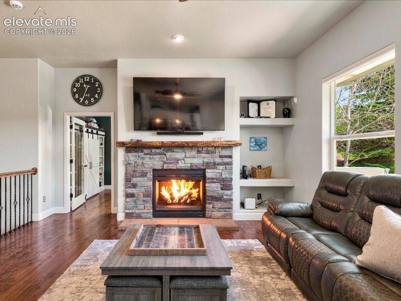 Image 20 of 50: Stone-clad fireplace with wood mantel, built-in shelving, wood-finish floor