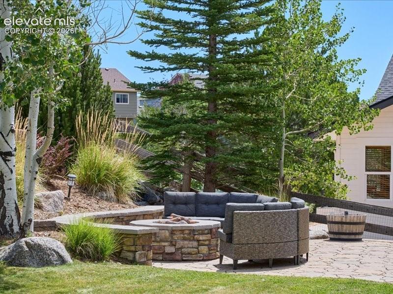 Image 39 of 50: Stone patio with a built-in stone fire pit, tiered landscaping with mature 