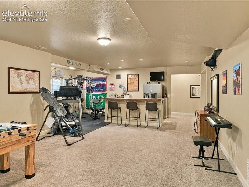 Image 44 of 50: Recessed lighting, wood-finish bar, and carpeted flooring define this versa