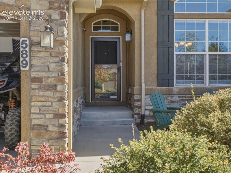 Image 8 of 50: Stone facade detailing, stucco exterior finish, arched entryway, multi-pane