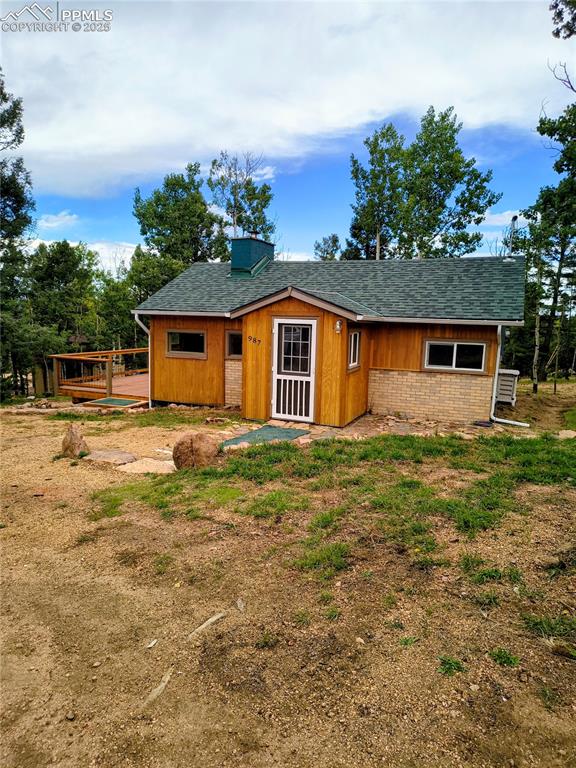 Caption: Rear view of property featuring roof with shingles, brick siding, a deck, and a chimney