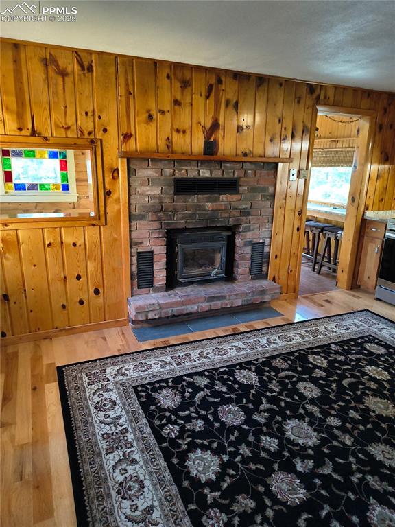 Image 10 of 20: Living room featuring wooden walls, wood finished floors, and a brick firep