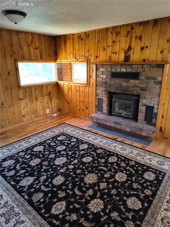 Image 11 of 20: Unfurnished living room with wood walls, wood finished floors, and a firepl