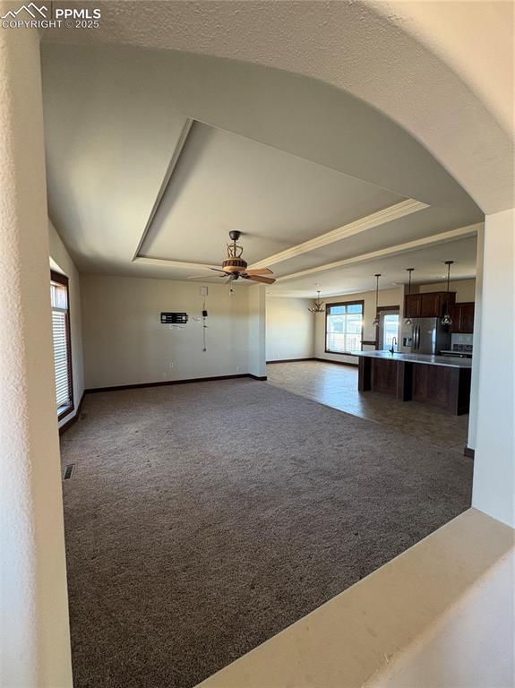 Image 9 of 32: Unfurnished living room featuring a raised ceiling, dark colored carpet, an