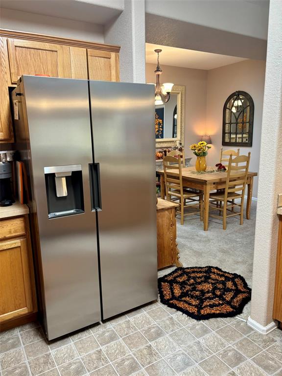 Image 12 of 24: Kitchen featuring stainless steel fridge, brown cabinetry, light countertop