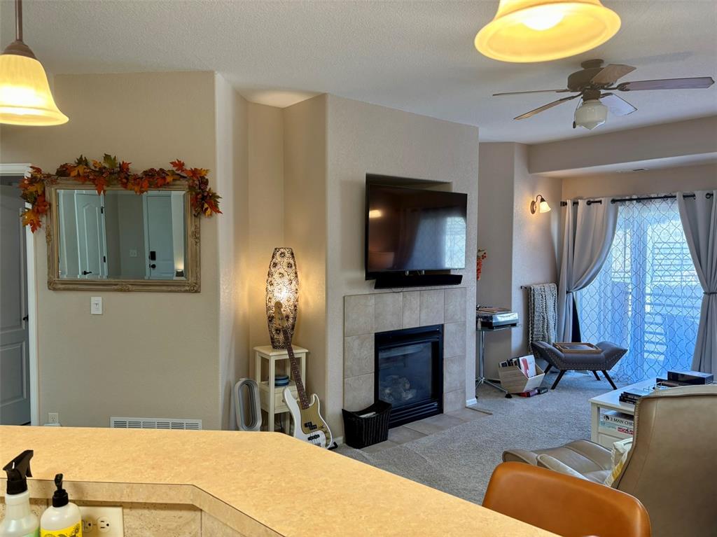Image 17 of 24: Living room with a tiled fireplace, a ceiling fan, and carpet