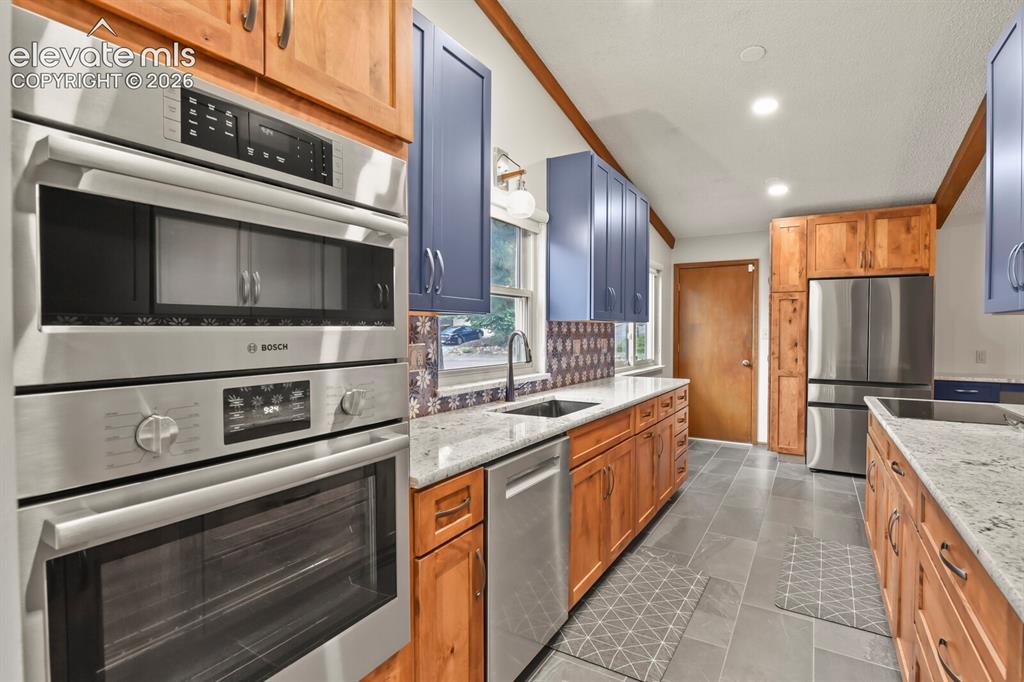 Image 11 of 50: Kitchen featuring granite countertops, wood cabinetry, blue upper cabinetry