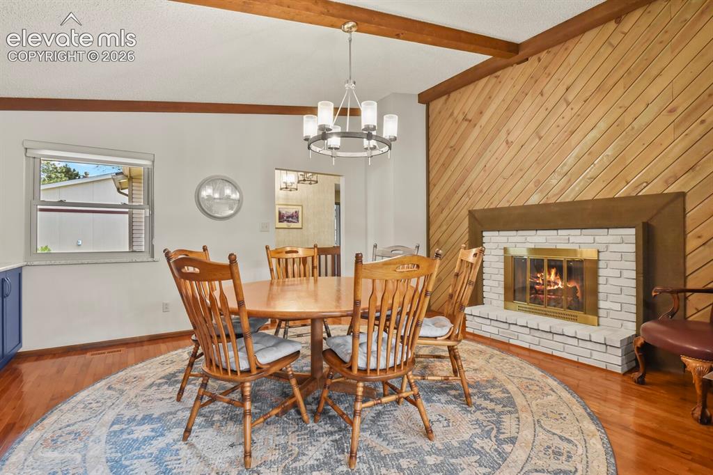 Image 16 of 50: Dining area featuring a white brick fireplace with a brass firebox, a diago