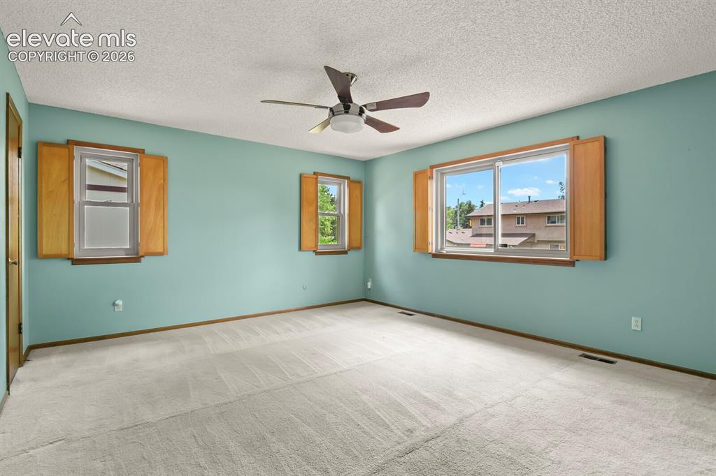 Image 18 of 50: Spacious interior room featuring light-colored carpet, three windows with w