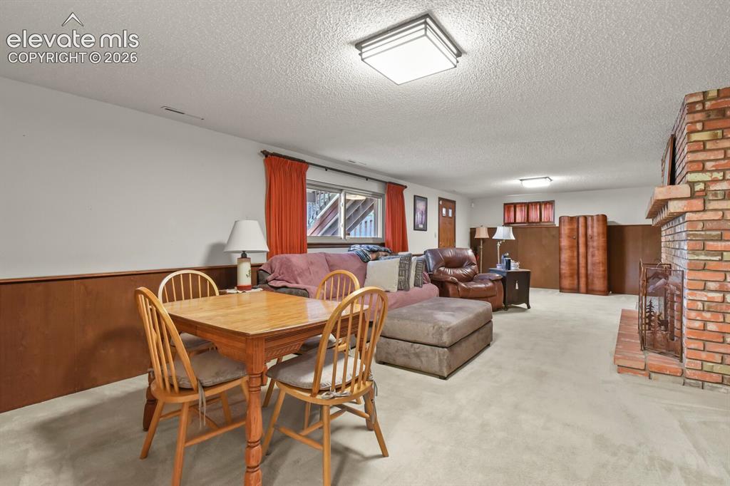 Image 25 of 50: Spacious room featuring a brick fireplace, wood-finish wainscoting, and whi