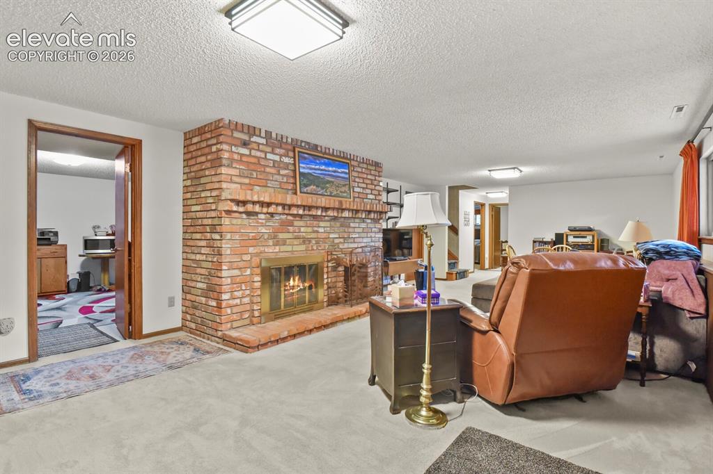 Image 26 of 50: Spacious room featuring a prominent brick fireplace with a brass firebox, l