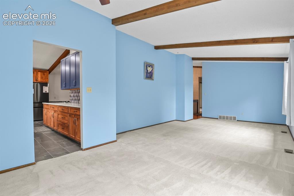 Image 9 of 50: Spacious room featuring light-colored carpeting, exposed wood ceiling beams