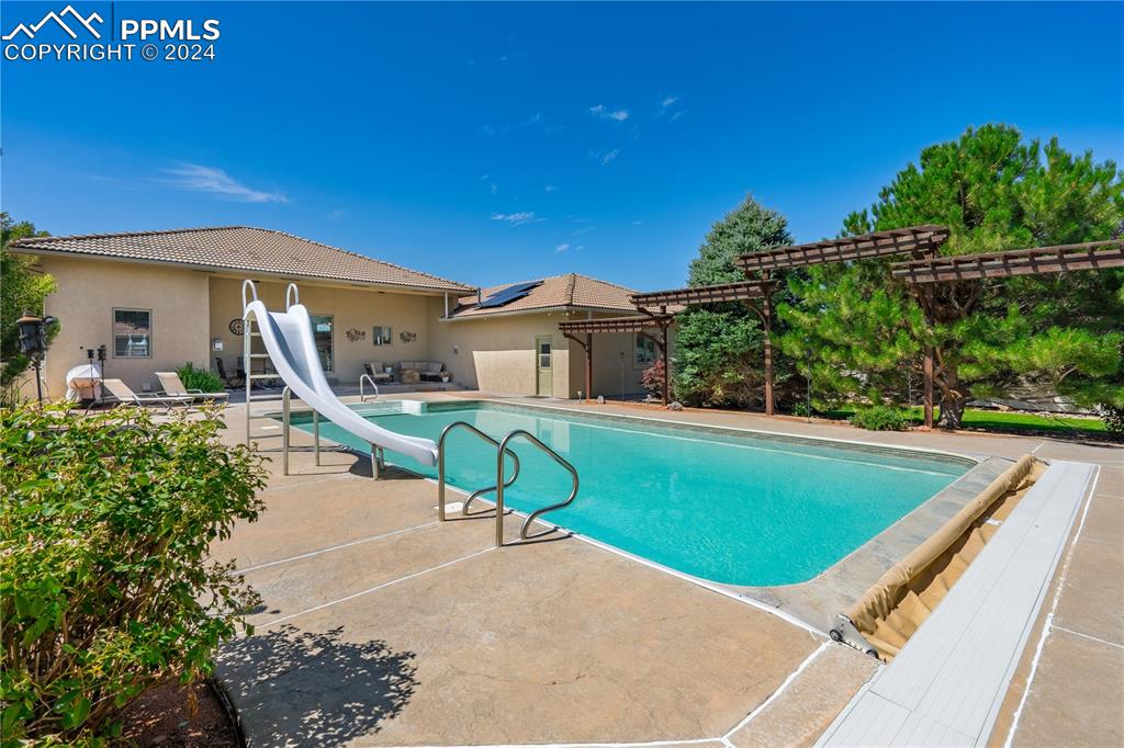 Image 35 of 39: View of pool with a patio, a water slide, and a pergola